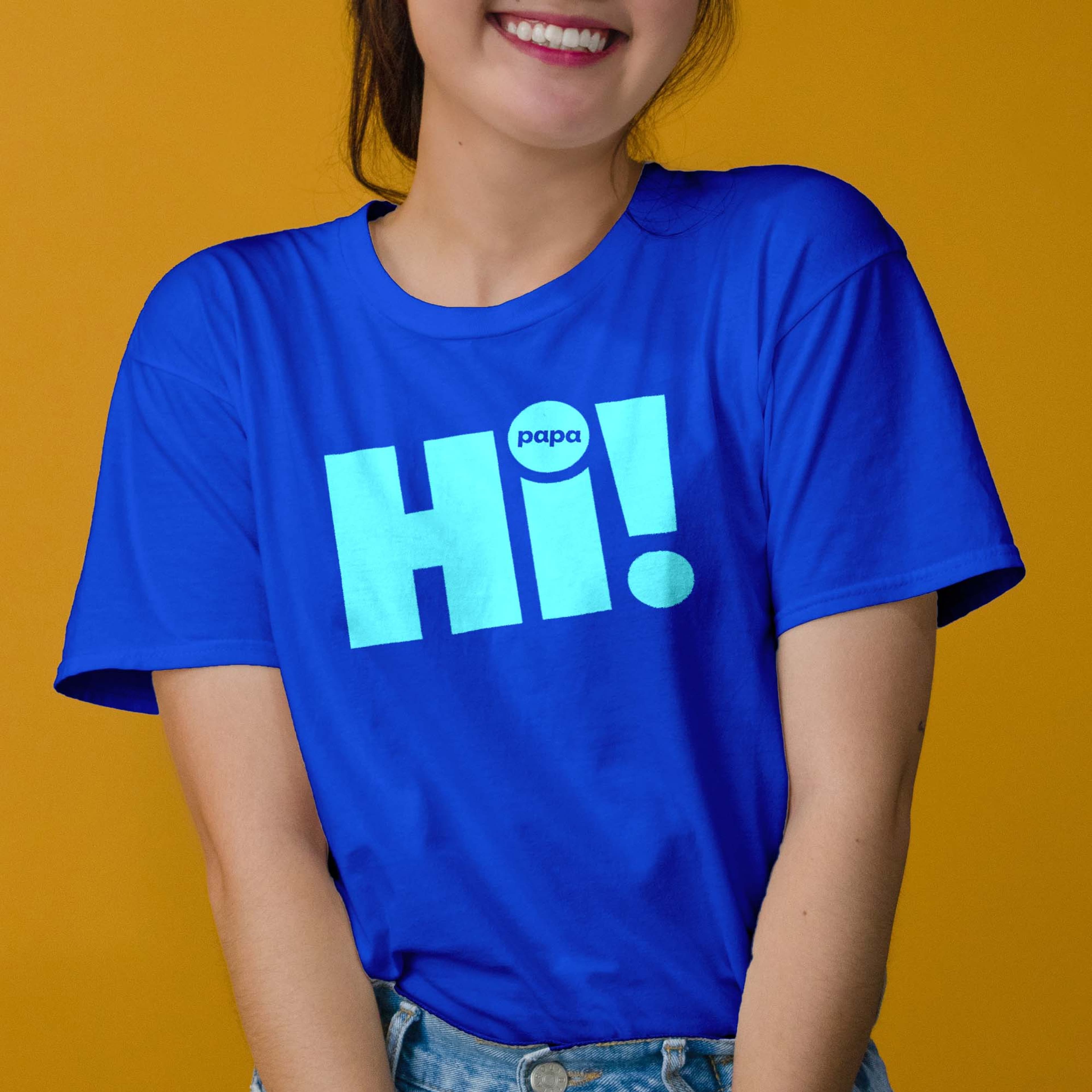 Person smiling and wearing a royal blue t-shirt printed with "Hi!" and "papa" in cyan text, against a yellow background.
