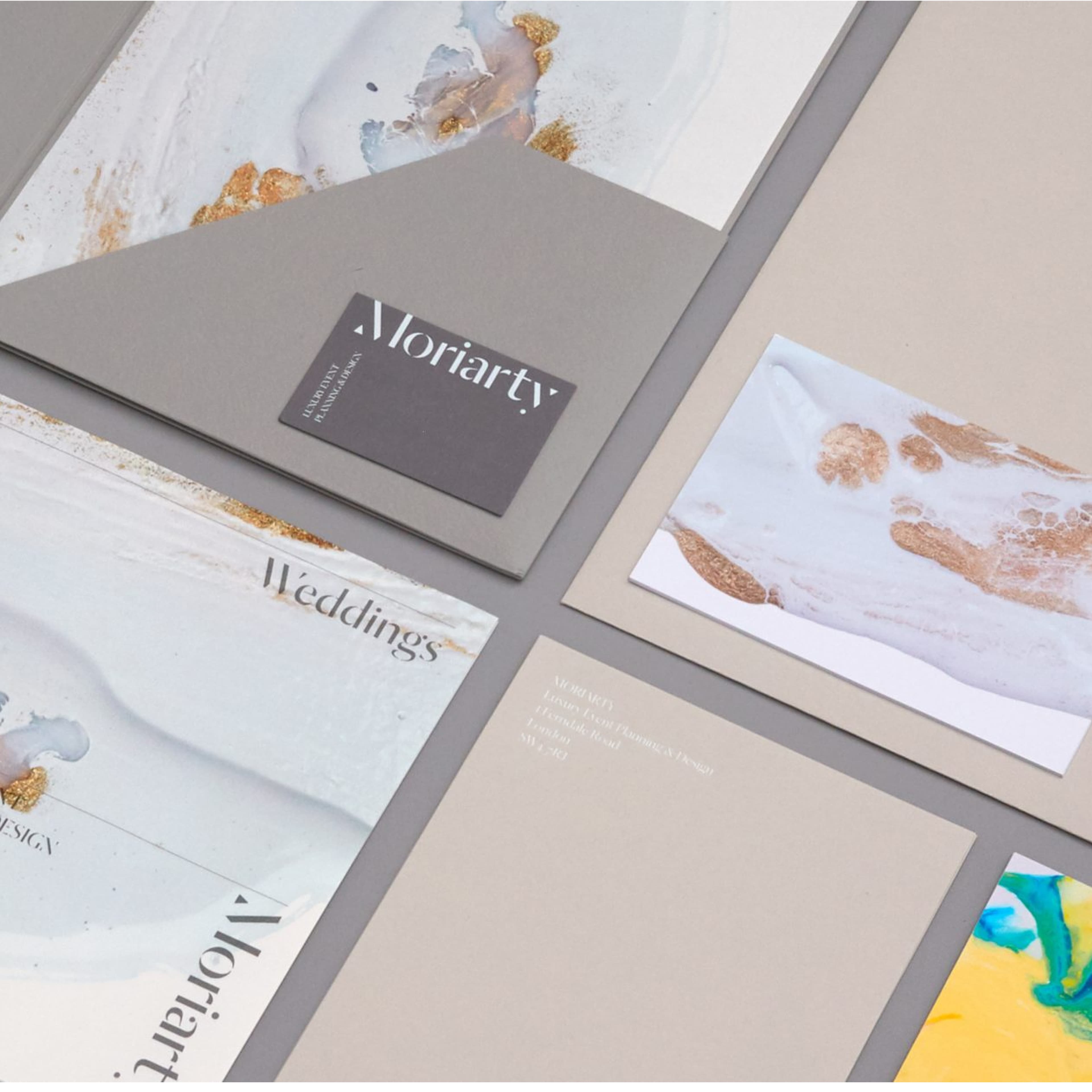 Moriarty Luxury Event Planning & Design branded stationery suite laid out flat, including a gray business card, folded brochures with "Weddings" text, and cards featuring white and gold abstract ink designs, with a London address visible on an envelope.