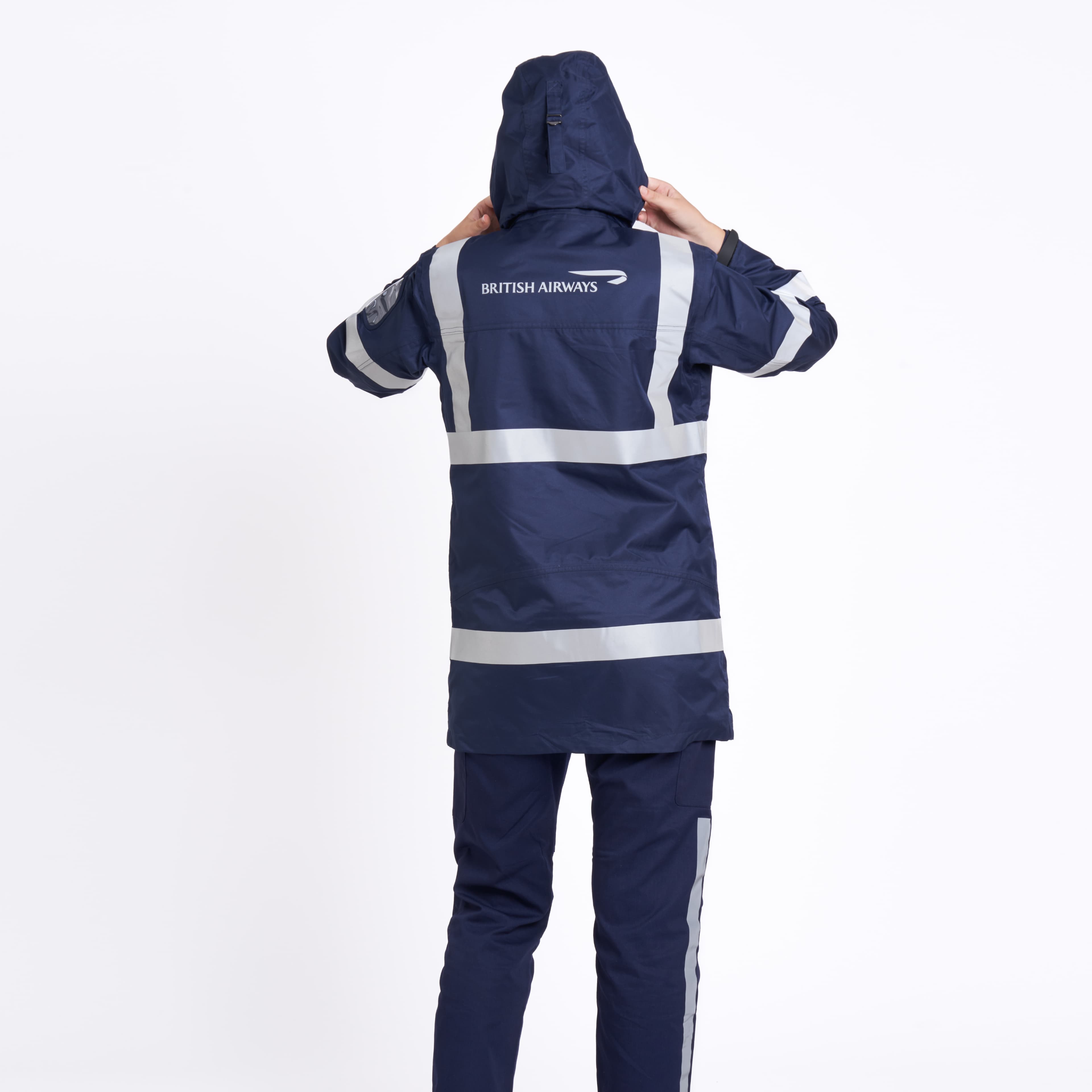 Person wearing a blue British Airways jacket with reflective stripes, viewed from the back, adjusting the hood against a white background.