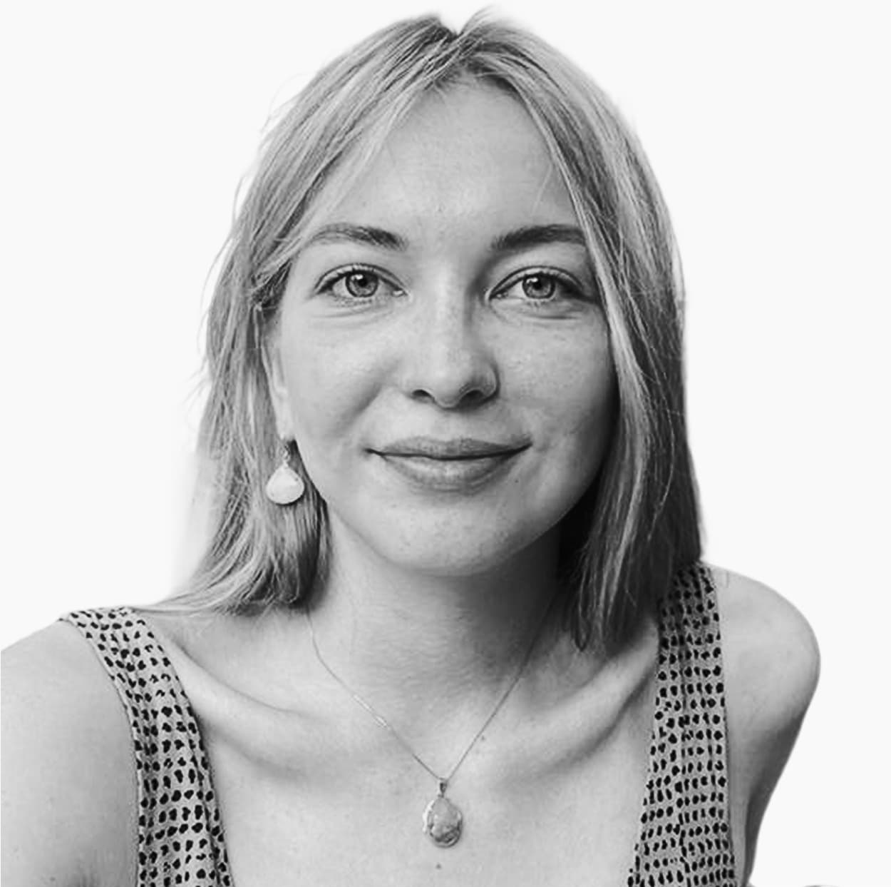 Young woman with light hair smiling at the camera wearing a dotted dress, necklace and drop earrings.