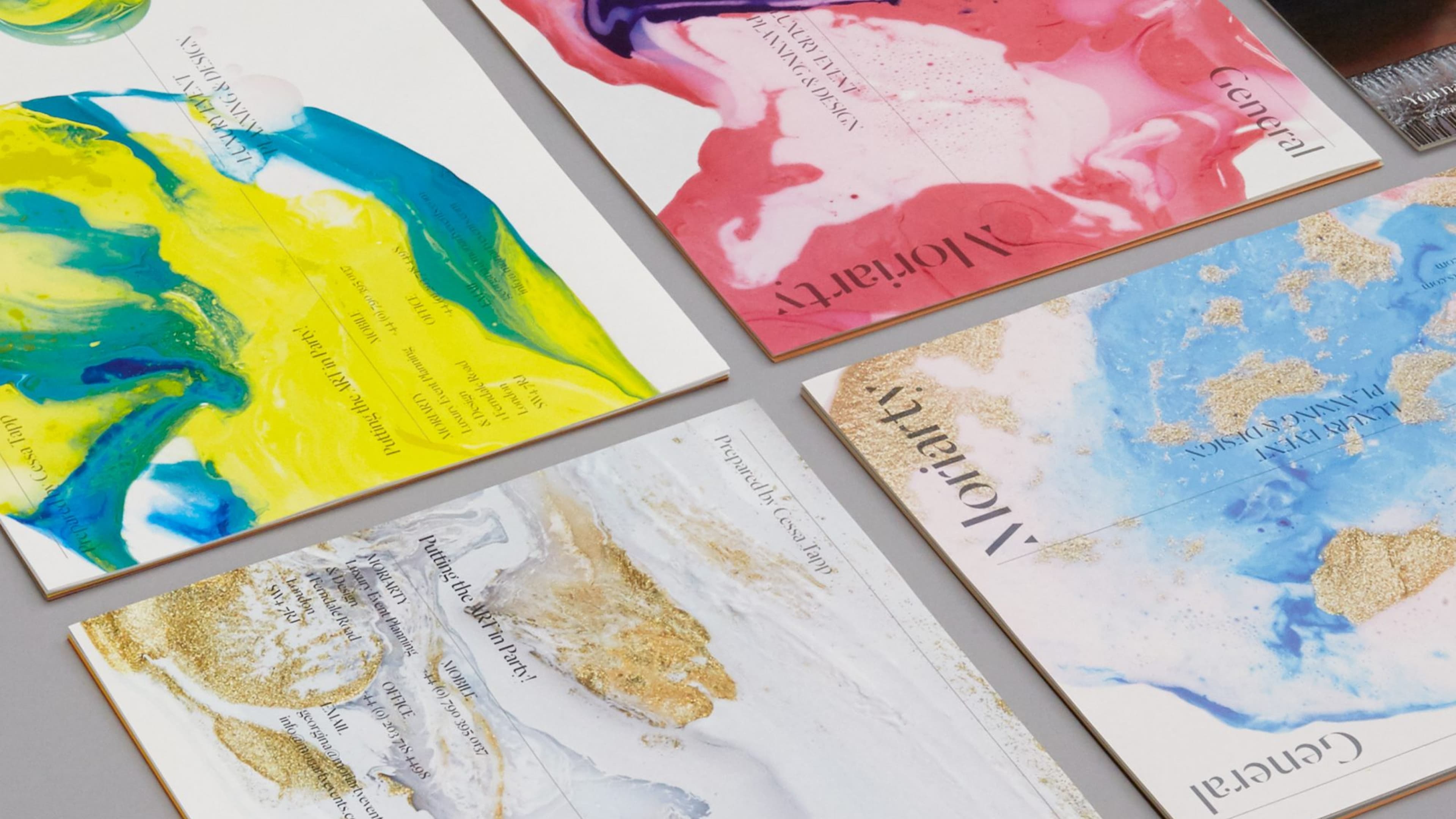 Five Moriarty Luxury Event Planning & Design brochures fanned on a gray surface, featuring vibrant abstract marbled designs in yellow-blue, pink-red, white-gold, and blue-gold colorways.