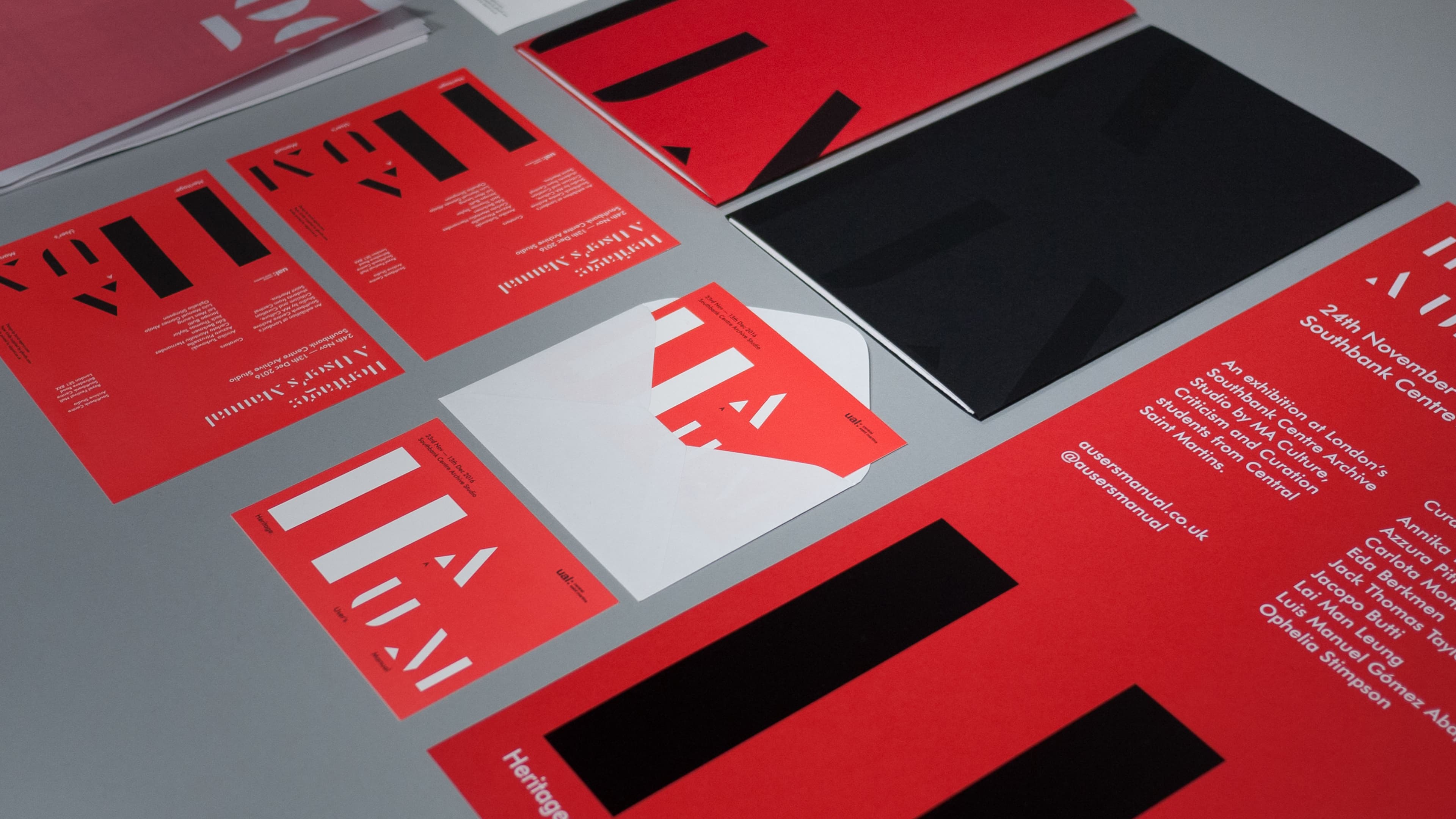 Printed collateral for "Heritage: A User's Manual," an exhibition at Southbank Centre Archive Studio by Central Saint Martins MA students, featuring red and black postcards, posters, and an envelope with bold typographic design, laid out on a gray surface.