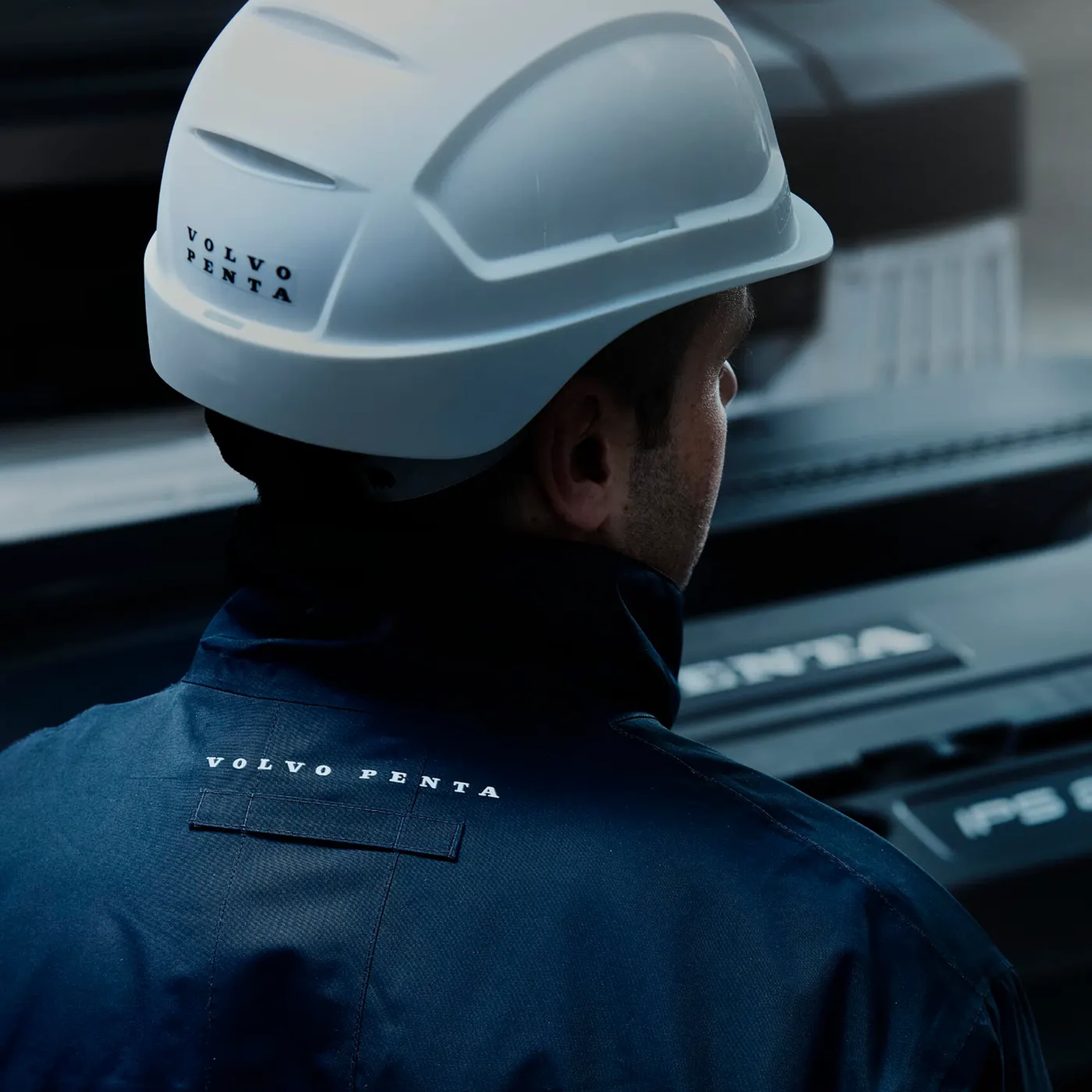 Picture of a man working wearing a blue jacket and white helmet both of which have the text Volvo Penta on the back.