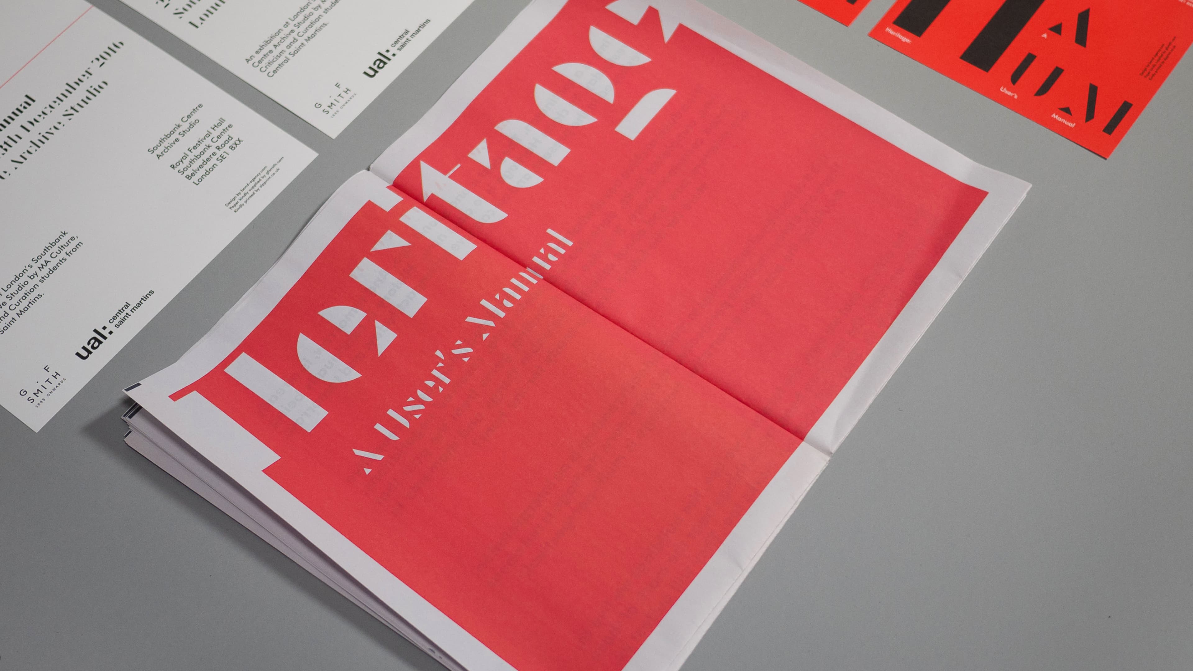 Printed materials spread on a gray surface, including an open red newspaper-style booklet titled "Heritage: A User's Manual" in bold white type, alongside white folded leaflets with black text referencing UAL Central Saint Martins.