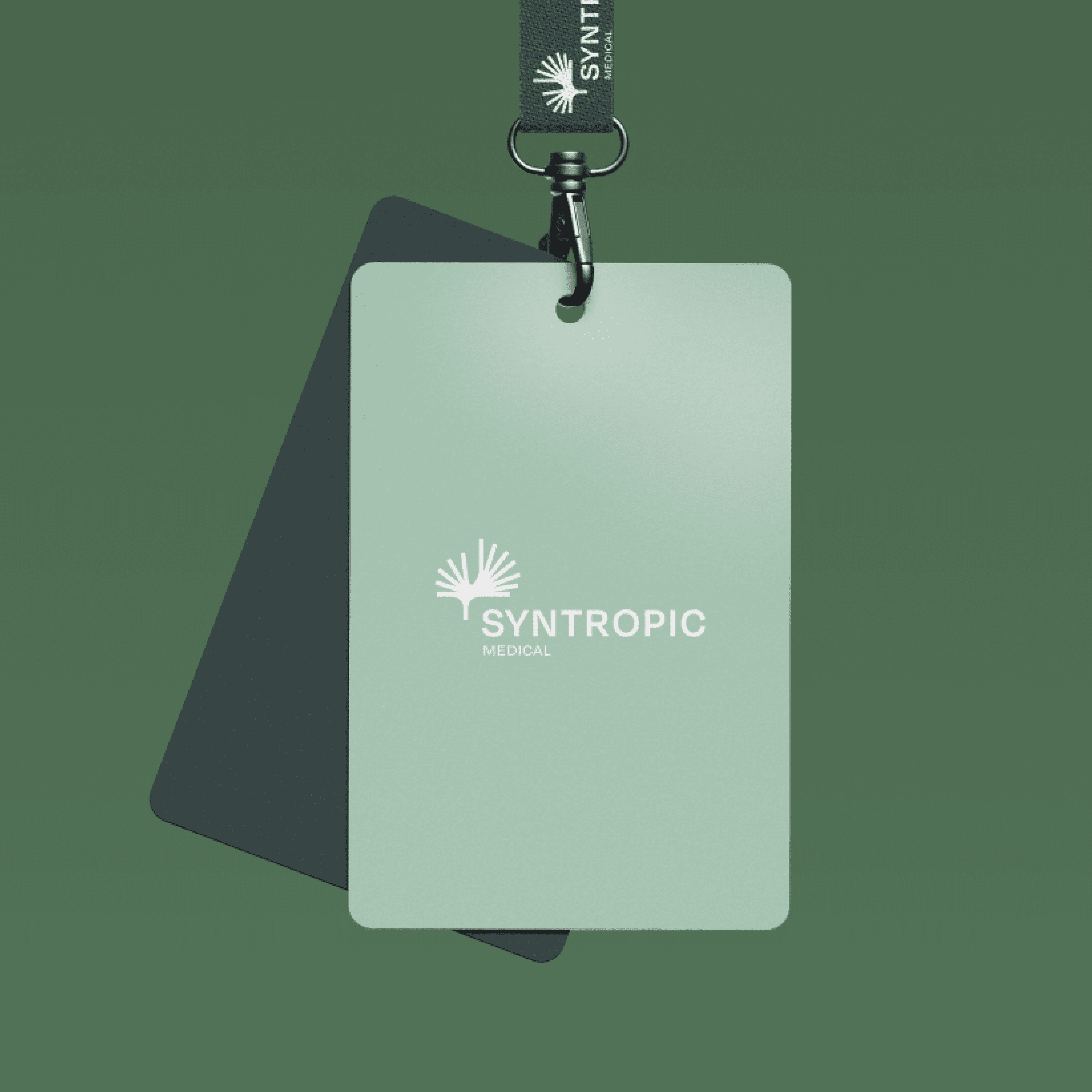 A green ID badge with 'SYNTROPIC MEDICAL' logo and a lanyard clip on a green background, alongside a dark green card.