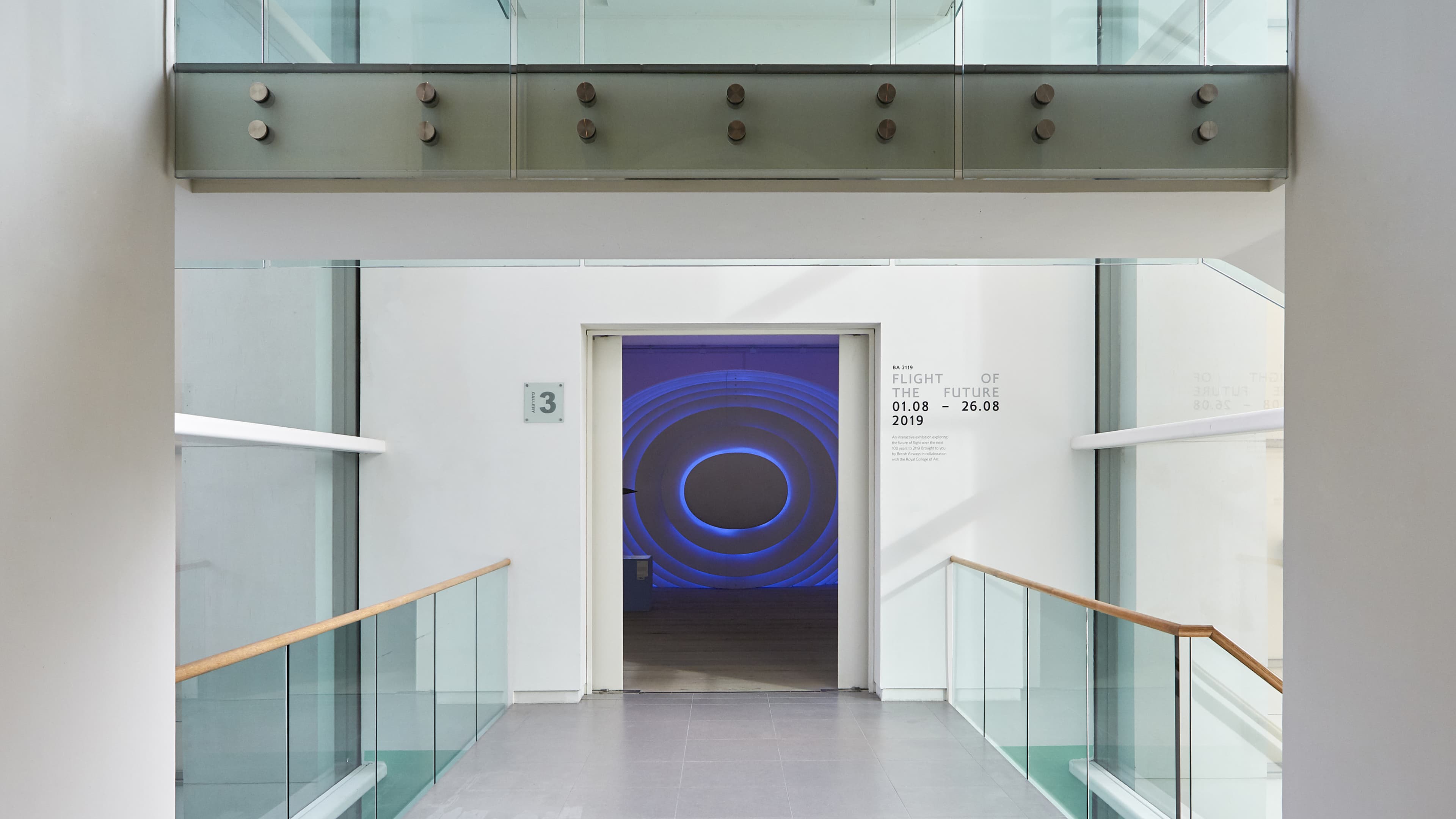 A modern gallery corridor with glass railings leads to an open doorway revealing a large wall installation of concentric glowing blue rings forming a portal-like ellipse. Wall text identifies the exhibition "Flight of the Future" (BA 2119), 01.08–26.08 2019.