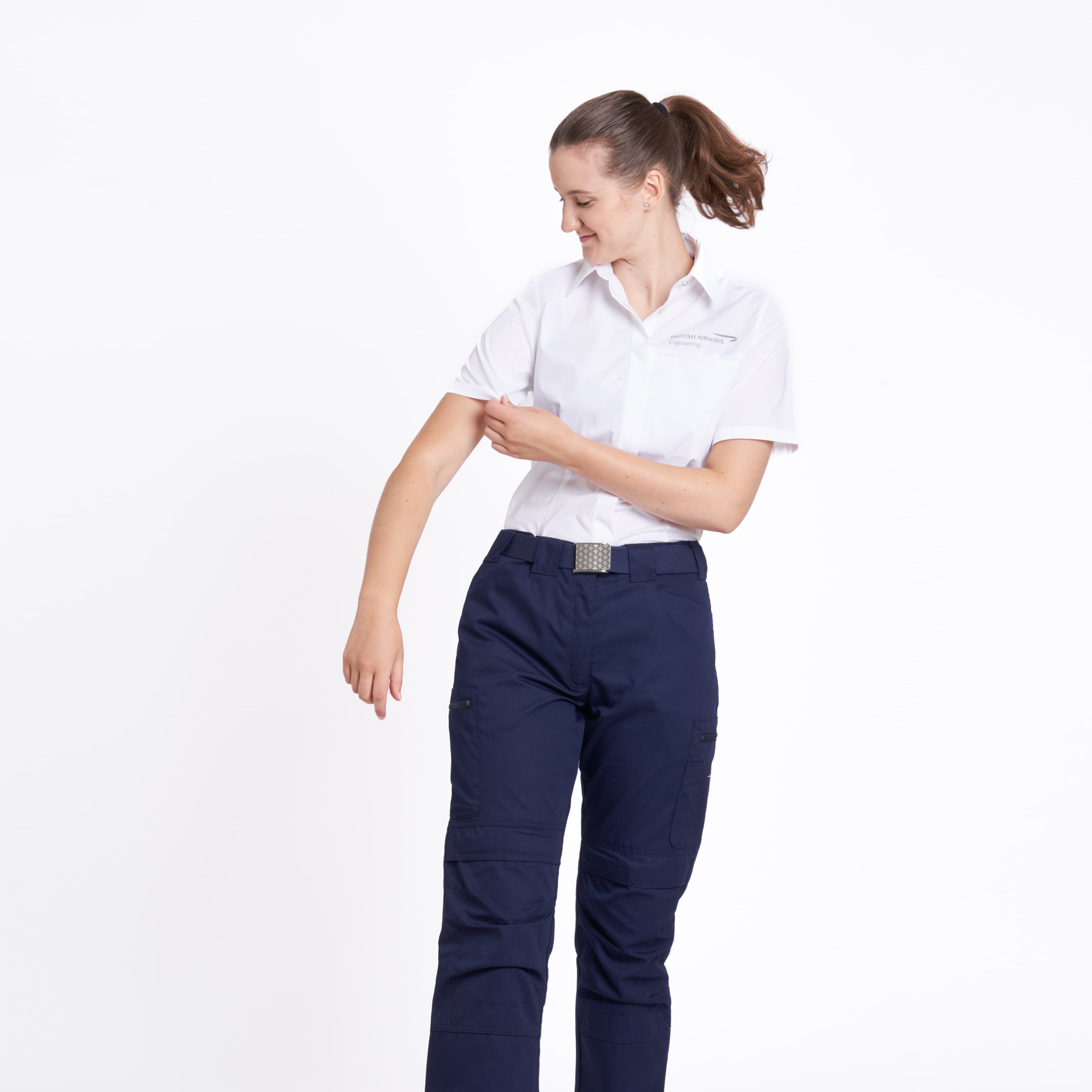 Woman in a British Airways Engineering white uniform shirt and navy cargo trousers adjusting her sleeve, against a plain white background.
