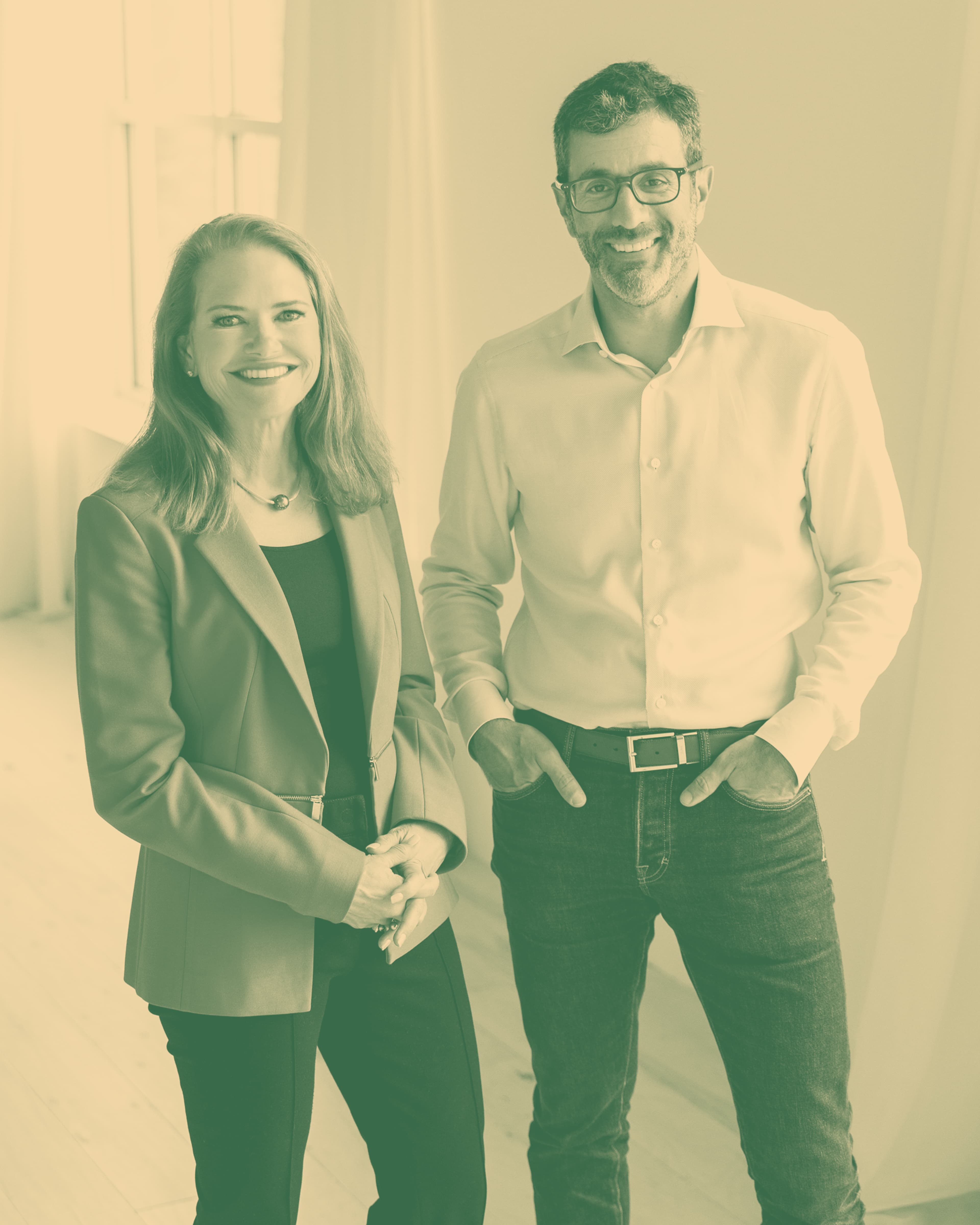 Amy and Brad smiling and standing together in a bright, open room with large windows.