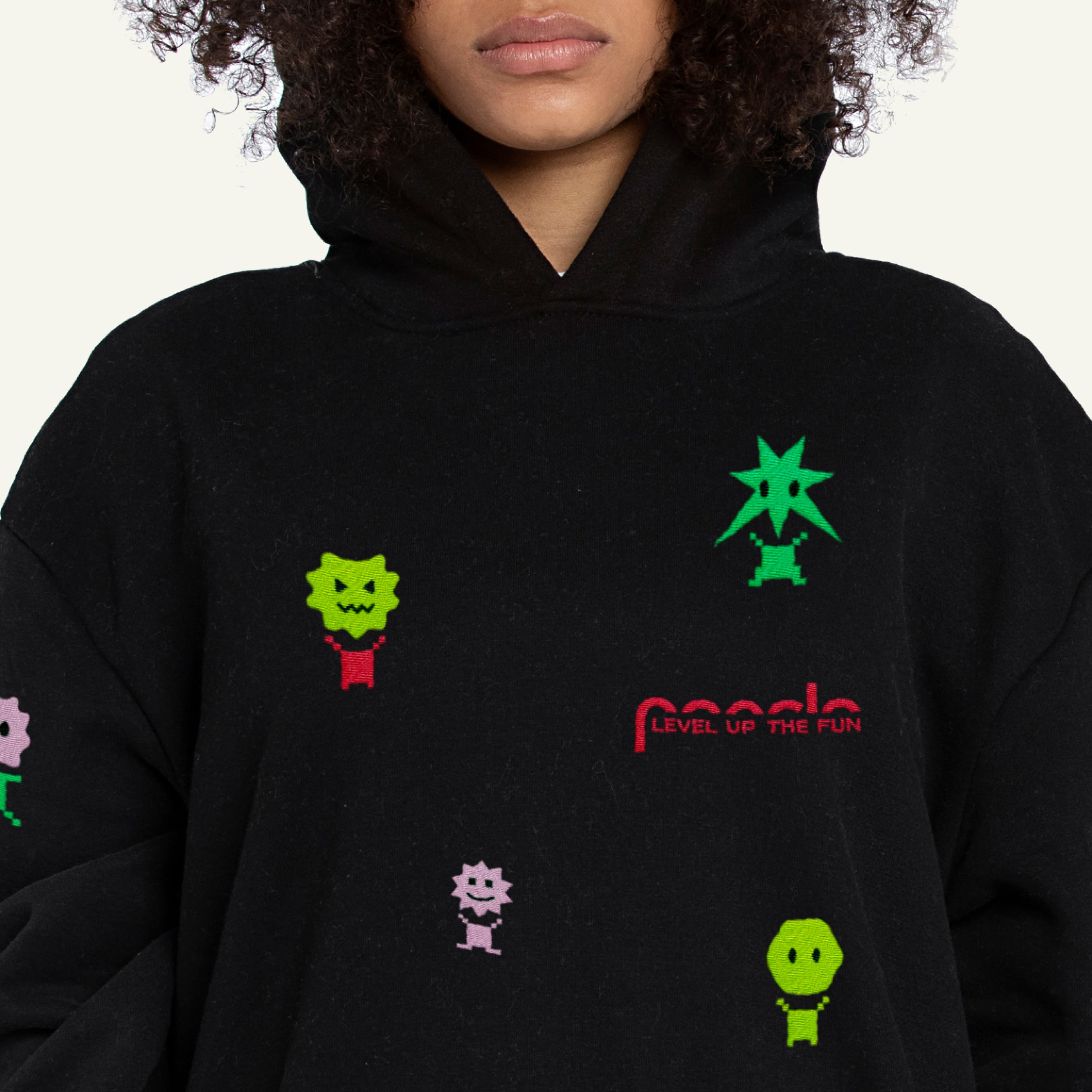 Black hoodie with colorful cartoon designs and text 'Level Up The Fun'. Woman with curly hair partially visible from the neck down.