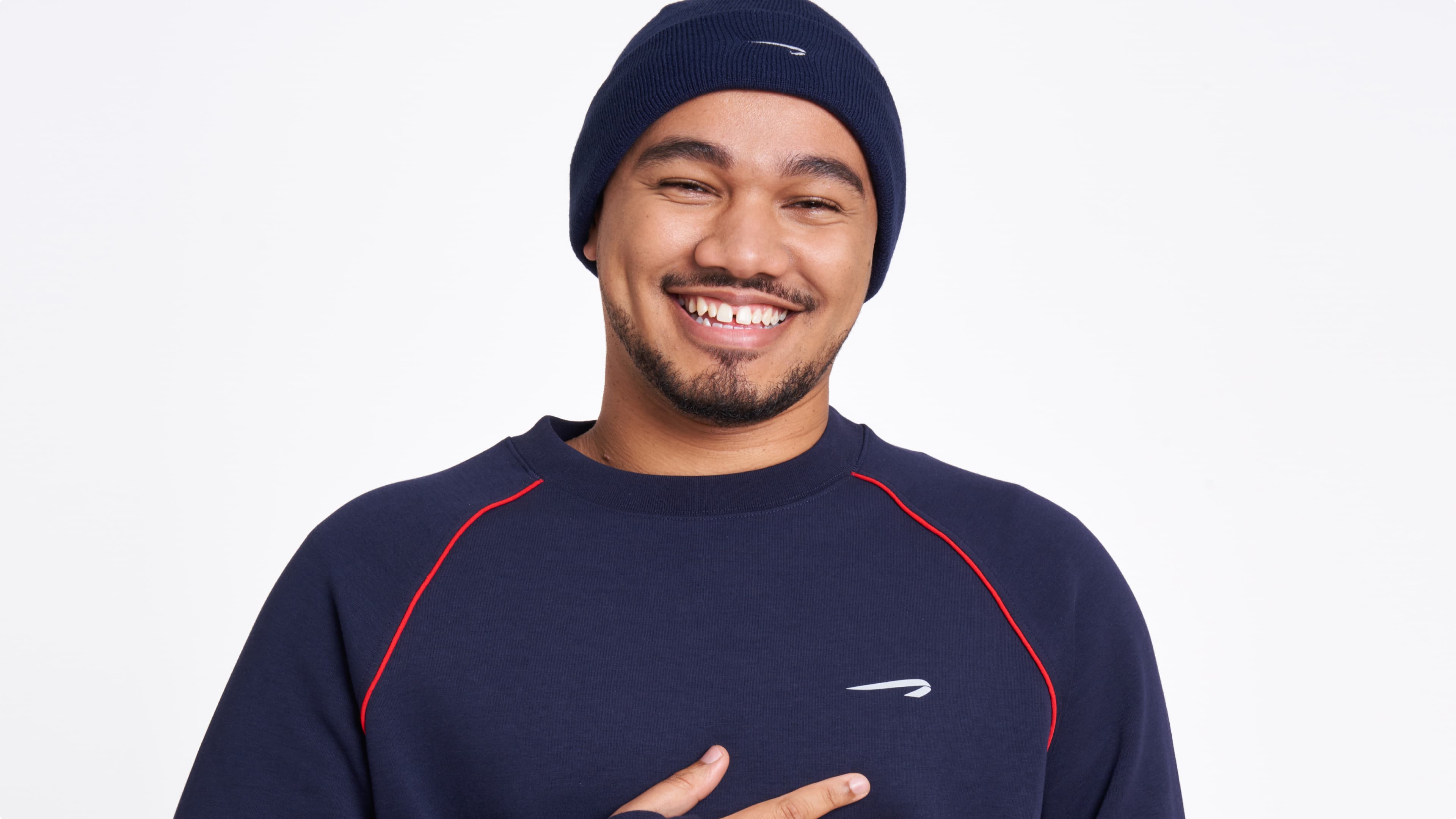 Person smiling warmly, wearing a navy blue beanie and sweater with red accents, featured in a Brooks Running campaign.