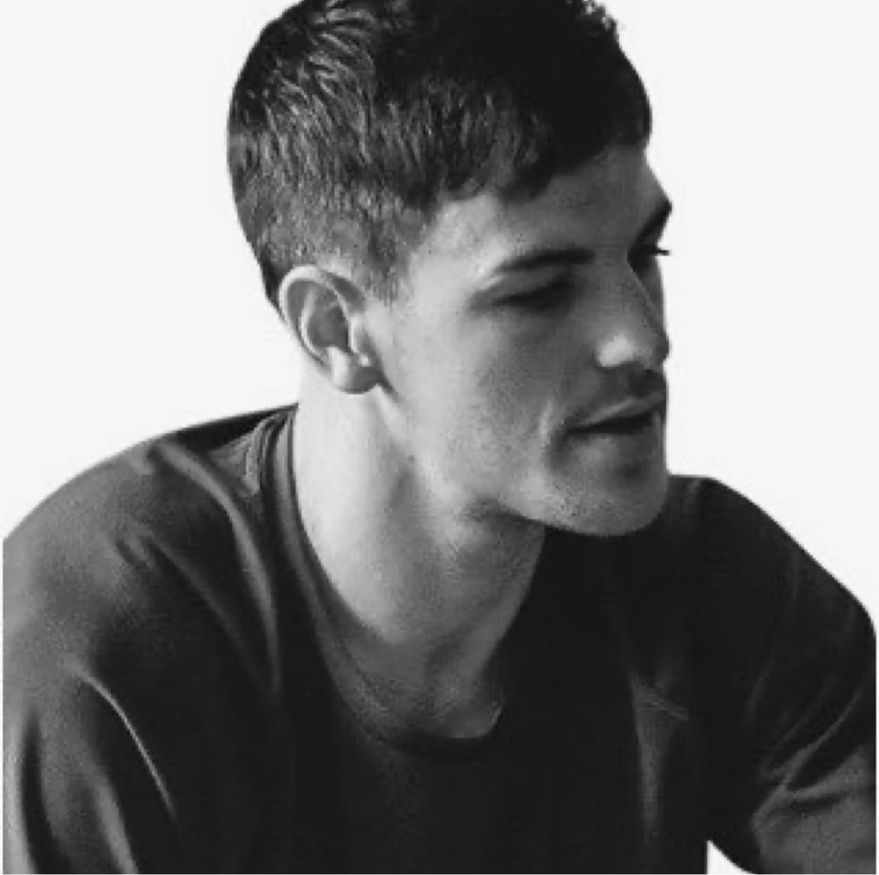 Young man with short dark hair looking to the side, wearing a dark t-shirt, in a black and white portrait photo.