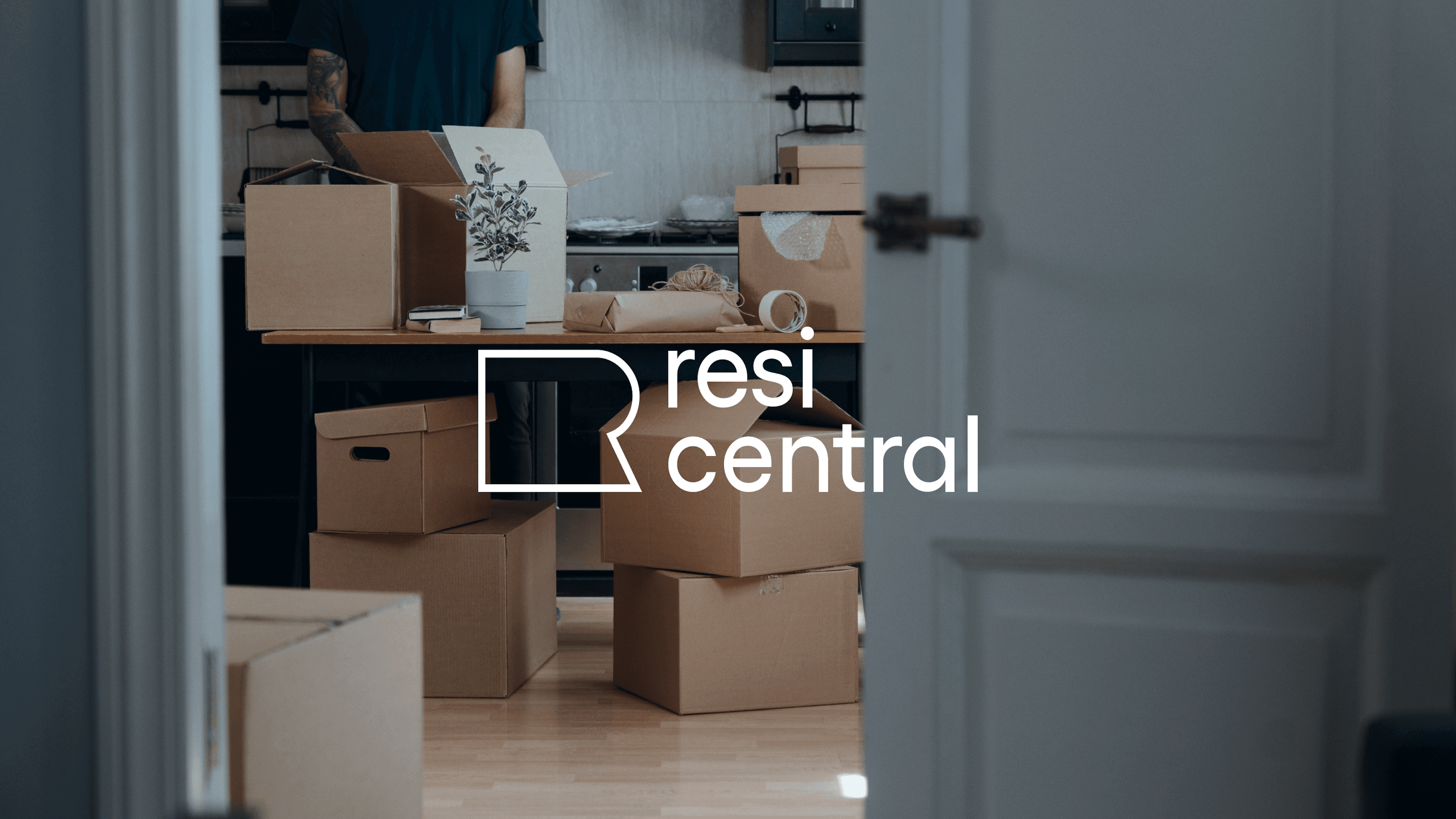 Resi Central logo overlaid on a photo of a person packing cardboard boxes in a kitchen, with packing tape and a small potted plant on a wooden table.